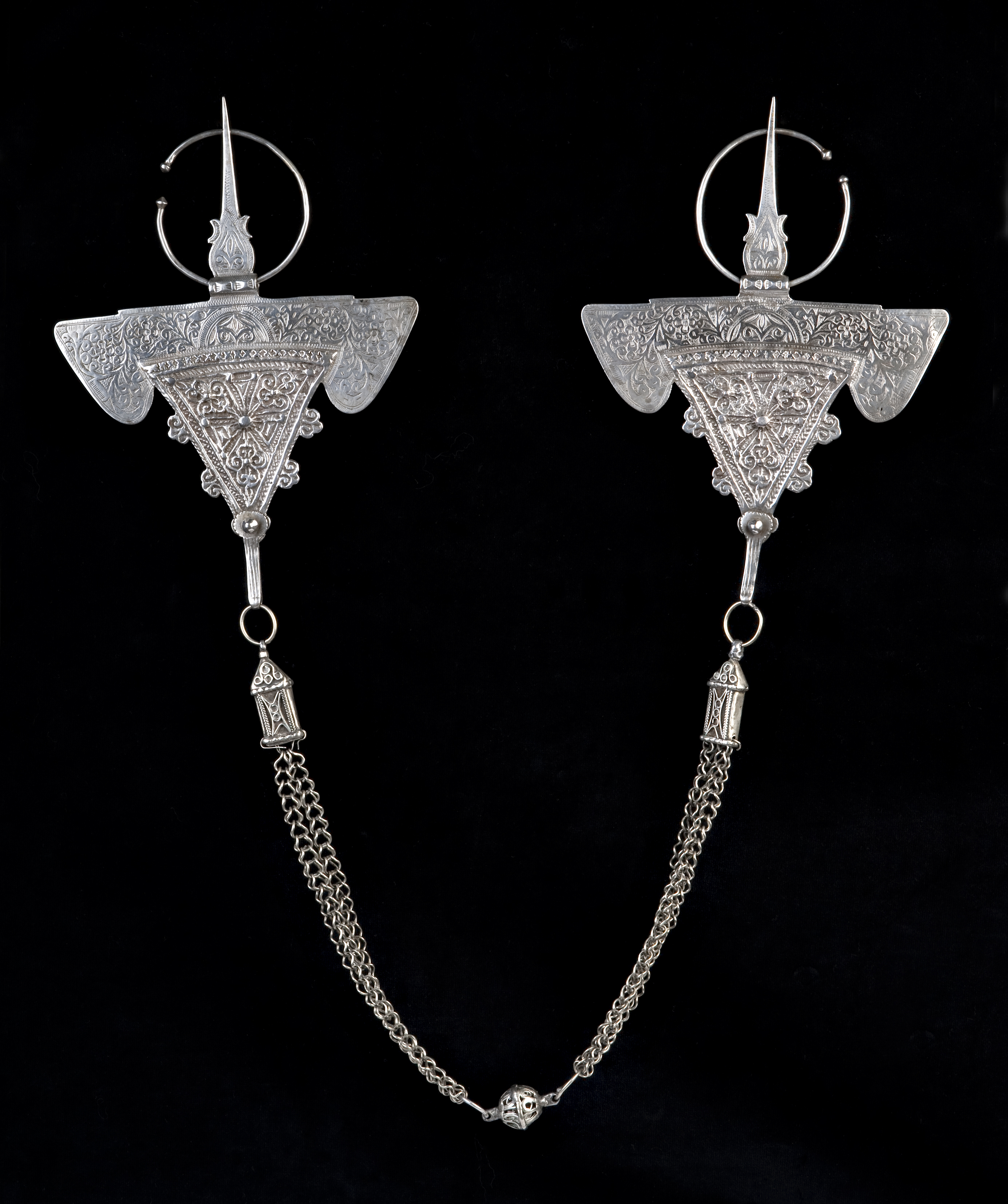 Parure pectorale : Paire de fibules [tizerzaï] et chaîne, dites fibules du « bélier ». Ihahen, région d’Essaouira. Fin XIXème – début XXème siècle. Argent. 17 x 14 cm ; largeur totale : 103 cm. Musée Pierre Bergé des arts berbères – Fondation Jardin Majorelle, Marrakech. © Musée Pierre Bergé des arts berbères – Fondation Jardin Majorelle, Marrakech ; photo : Nicolas Mathéus