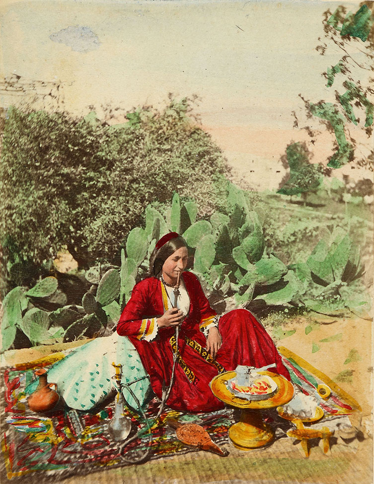 Charles Lallemand, Ludovico Hart, Femme chrétienne de Zouk Mikael (Liban septentrional) fumant le narguilé et préparant le café sur la terrasse d'une maison, vers 1863-1865. Tirage sur papier albuminé d'après négatif sur verre, rehauts de peinture, 29 x 22.5 cm. Publié dans Galerie universelle des peuples de Syrie, éditeur A. Varroquier & Cie. Collection Fouad Debbas / Musée Sursock © Collection Fouad Debbas / Musée Sursock